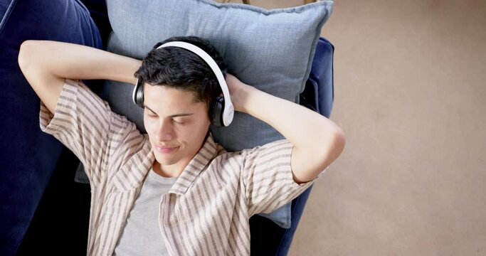 High angle of happy biracial man in headphones lying on couch with eyes closed, slow motion