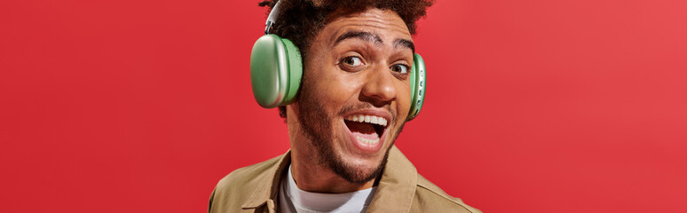 banner of excited african american man in wireless headphones with open mouth on red background