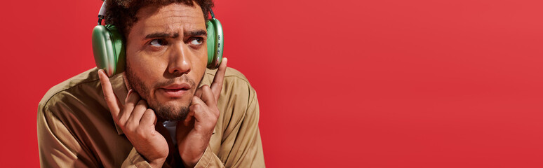 banner of confused african american man in wireless headphones listening music on red background