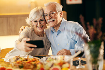 A happy senior couple is taking selfies on lunch table at home.