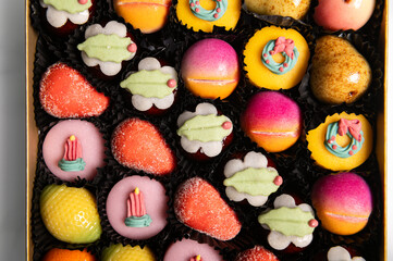 Box of rainbow marzipan sweets in form of different fruits and cakes