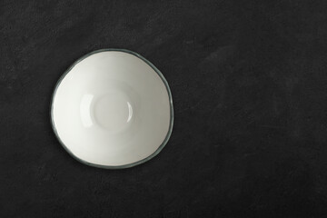 Handmade empty ceramic plate top view with copy space on dark concrete table. Minimalism. Eco friendly ceramics handcraft tableware.