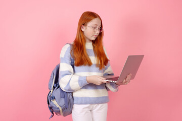 Naklejka premium Confident redhead teenage girl with bag and laptop wearing glasses on pink background in studio.