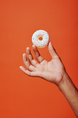 Fototapeta na wymiar cropped shot of man holding glazed vanilla donut with sprinkles on orange background, white icing