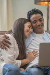 Happy young relaxed couple sitting on sofa with laptop on laps, discussing funny movie, enjoying watching comedian film, shopping online or web surfing, full length front view, leisure pastime concept