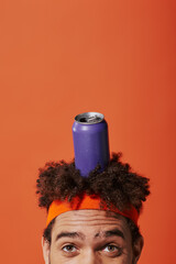 purple soda can on head of curly african american man with headband on orange background
