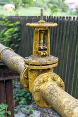 Fototapeta premium Gas pipe with big old valve-crane. Industrial gas pipeline laid along fence, gasification of population.
