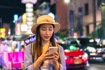 Young Asian woman traveler tourist using a mobile phone in China town night market in Bangkok in...