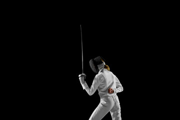 Female fencer stands at ready, her blade held high, poised to strike, but she waiting, her...