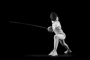 Fencer lunges forward, her blade in motion against black studio background. She is focused and...