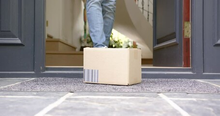 Low section of biracial man picking up delivery in cardboard box outside front door, slow motion