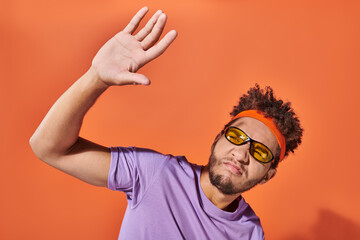 african american man in eyeglasses pouting lips and covering face from light on orange background