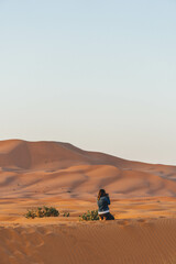 woman taking pictures of big sand dunes in the desert morocco with orange color view and arid vegetation