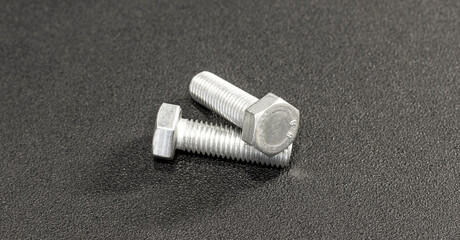 Close-up of two hexagon bolts against a black backdrop. The hexagon bolts stand out with their...