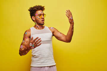 surprised african american man looking at stickers on his hands and body on yellow background