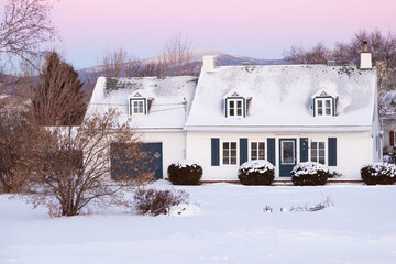 Sunrise winter view of beautiful patrimonial white clapboard house with steep shingled roof and...