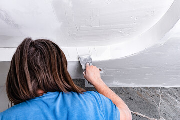 Female painter applying putty to ceiling.