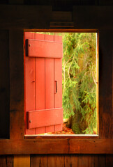Opened red shuttered window from inside a New England barn to the outside. Shutter halfway open.