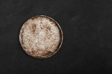 Handmade empty ceramic plate top view with copy space on dark concrete table. Minimalism. Eco friendly ceramics handcraft tableware.