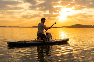 Man paddle boarding at lake during sunset together with pug dog. Concept of active tourism and...