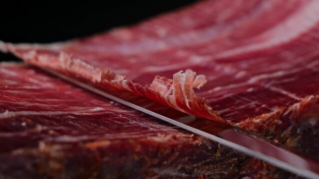 Knife cutting slicing a traditional Iberico Spanish ham, jamon. Whole leg. Close up