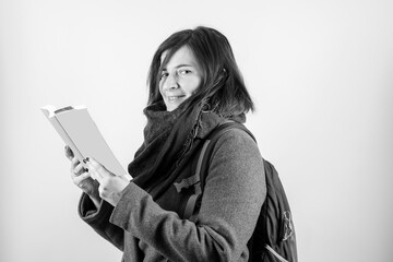 Attractive woman looking at the camera reading a book, in black and white, and with gray background. Concept of book reading.