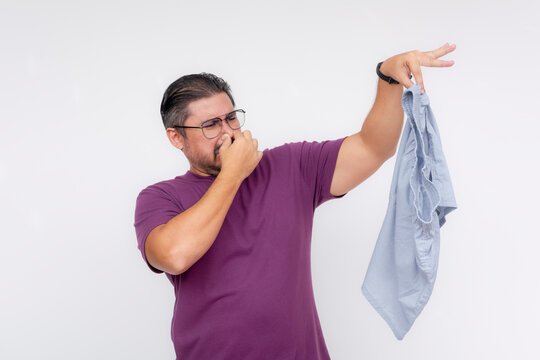 A disgusted middle aged man covers his nose while holding a stinky and smelly pair of boxer shorts with his hand. Isolated on a white background.