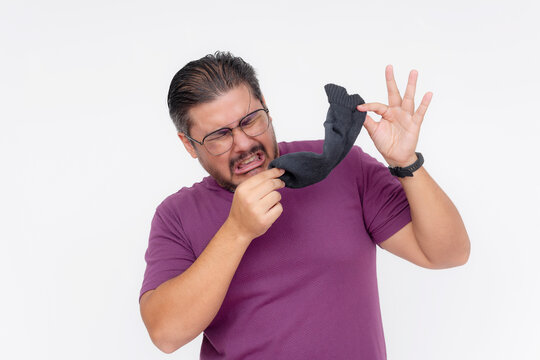 A middle aged man grossed out by the bad smell of a stinky sock in his hand. Exaggerated action depicting dirty laundry. Isolated on a white background.