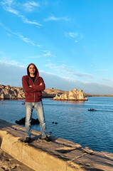 Young man standing at the nile river bank in aswan with cloudy sky in winter at sunset, Egypt.