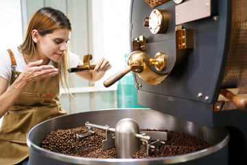 Professional coffee roaster working with modern automated roasting machine in the coffee roasting...