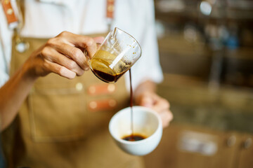 Professional Asian female barista pouring a shot of espresso into a coffee cup close up. Happy female barista making a cup of espresso coffee in a small coffee shop. Small business concept.