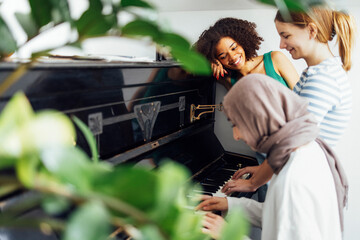 Cute smiling female teenagers play duets on the old piano. Caucasian, afro american and muslim...