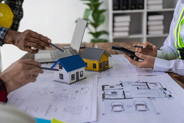 A team of construction workers and engineers meet to plan home construction and plan an office...
