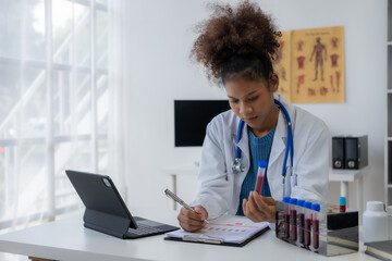 African American female doctor doing research wearing gloves looking at blood test tube in her hand...