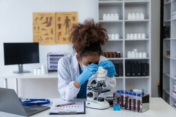 African American female doctor doing research wearing gloves looking at blood test tube in her hand...