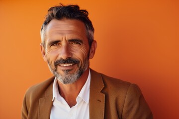 Handsome mature man looking at camera and smiling while standing against orange background