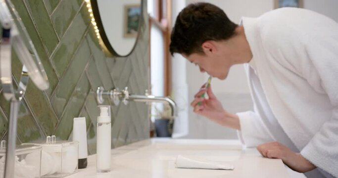 Biracial man brushing teeth in morning in bathroom, copy space, slow motion
