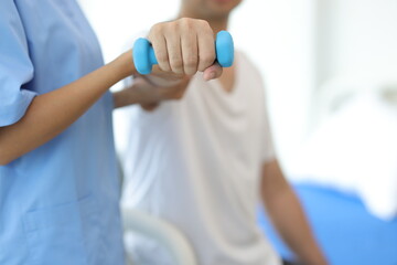 Nurse in an examination room at a hospital is doing physiotherapy for a male patient's arm with...