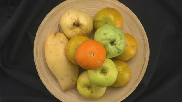Top view rotation of various tropical fruit in bamboo tray on black cloth background.