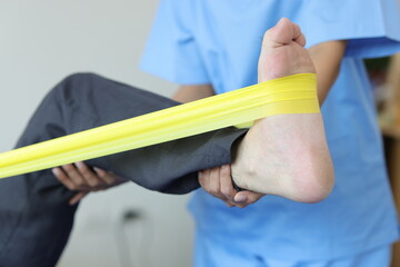 Fototapeta na wymiar Physiotherapist nurse treating patient with exercise using elastic band therapy rehabilitating man leg. Concept of physical therapy and rehabilitation.