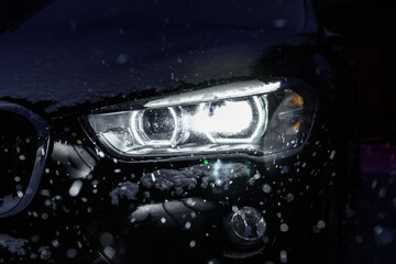 Night driving in winter. Front headlight of car glowing in dark in snowfall. © Natallia