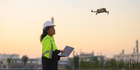 female engineers wearing uniforms and helmets fly drones to inspect petroleum industry projects.