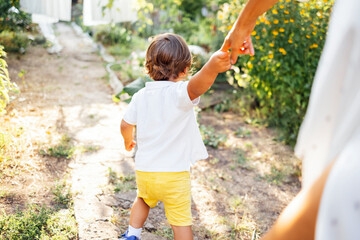 Little boy toddler is walking hand in hand with his mother along path in garden.