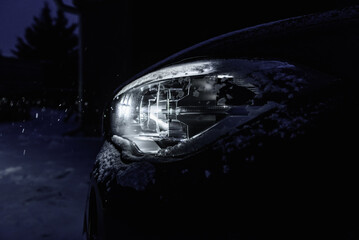 Night driving in winter. Front headlight of car glowing in dark in snowfall.