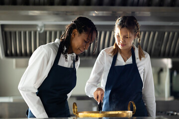 portrait two young african and caucasian woman cooking student. Cooking class. culinary classroom. group of happy young woman multi - ethnic students focusing on cooking lessons in a cooking school.