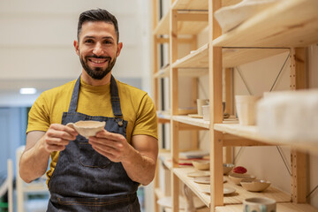 Hispanic man looking at the camera with his apron showing a mug inviting you to start classes in a...