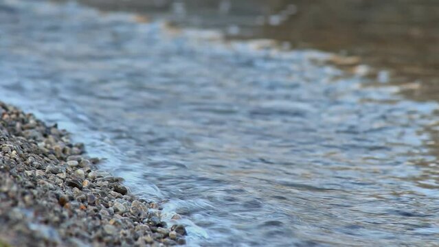 Shoreline pebbles washed by gentle waves of Black Sea, clear water ebbs on Crimean beach, tranquil summer season scene. Pebbled coast close-up, serene nature, tourism, travel to Crimea.