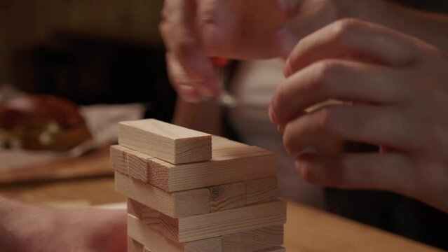 Group of Diverse Cheerful friends having fun together at a restaurant. Guys Playing Board Game Jenga at bar. Close up in slow motion