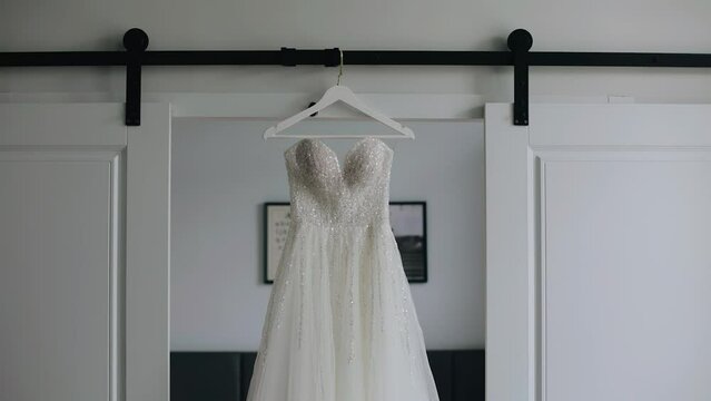 A white wedding dress is hanging on a hanger in the doorway. The camera moves smoothly while taking pictures of the object