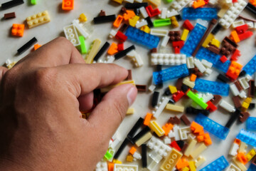man hand arranging pile of colorful Lego blocks. Top angle view of hand holding lego bricks on white background - obrazy, fototapety, plakaty